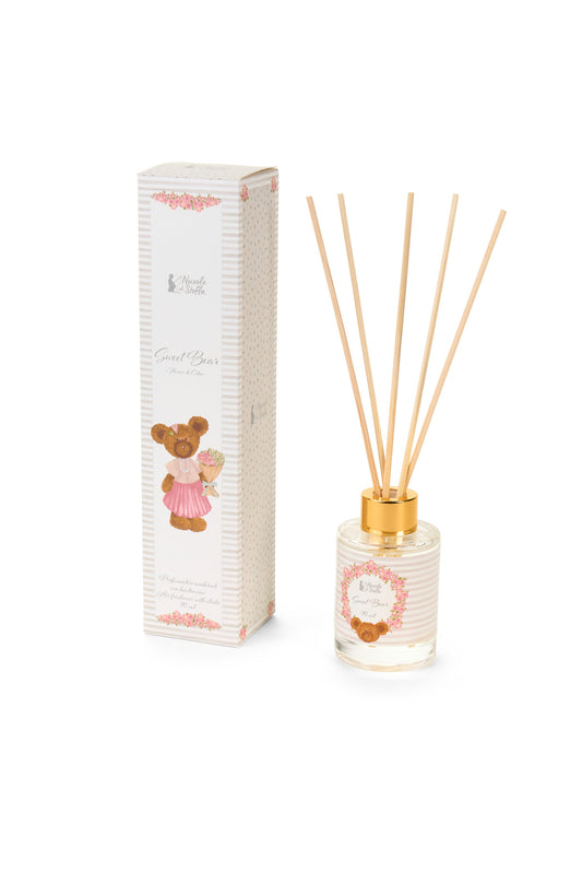 Profumatore per ambienti con bastoncini della collezione "Sweet Bear" di Nuvole di Stoffa, completo di boccetta in vetro da 70 ml e confezione regalo coordinata. Il diffusore presenta una delicata trama a righe bianche e rosa con l'illustrazione di un tenero orsetto e una ghirlanda di fiori, rifinito da una ghiera dorata, ideale per profumare e decorare le camerette dei bambini o come idea regalo.