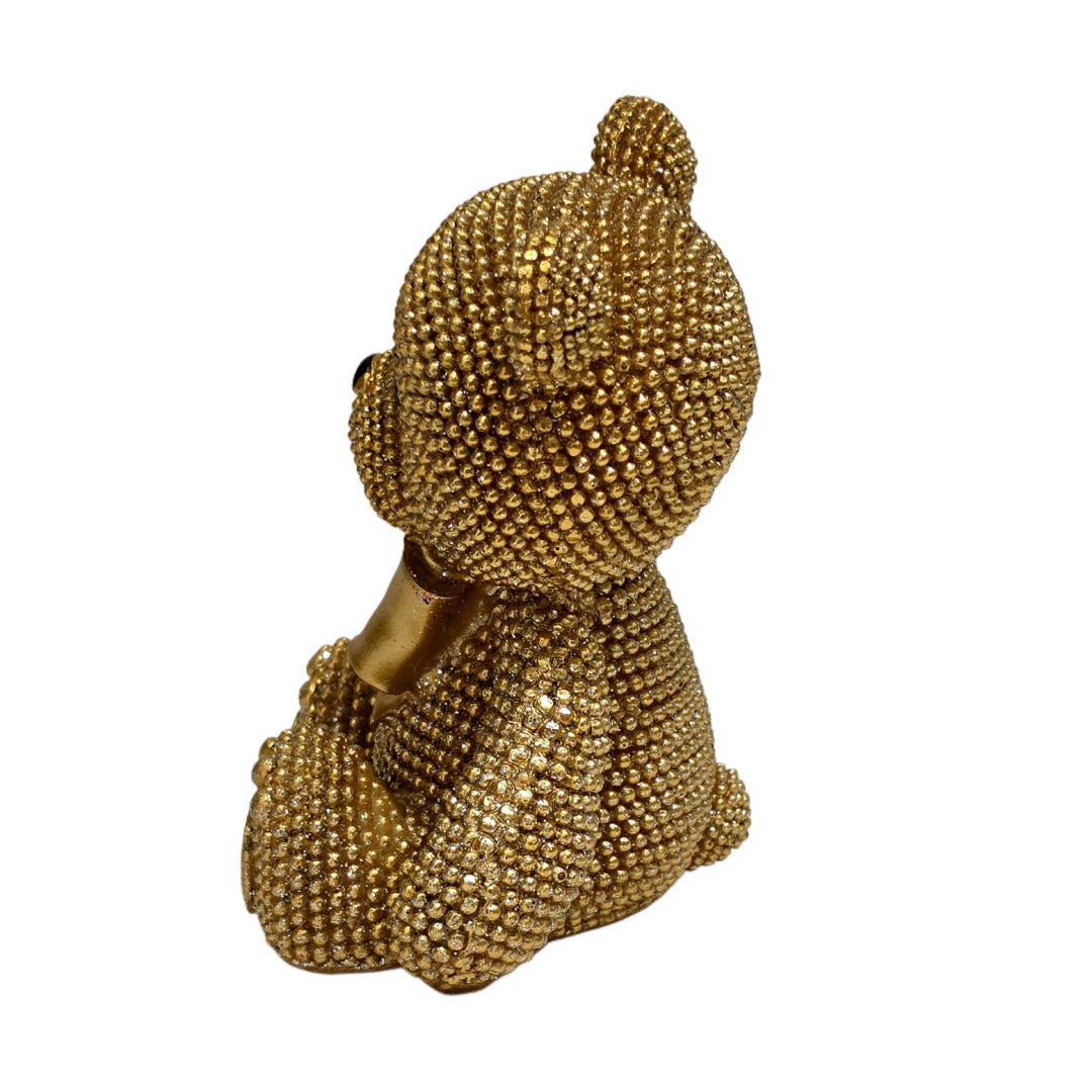 Statuina orsetto in resina dorata interamente ricoperta di brillantini glitterati, con fiocco raso oro al collo, occhi e naso neri e cuciture in rilievo sulle zampe. Oggetto decorativo scintillante firmato Sud Import, ideale come soprammobile glamour o idea regalo per bambini e occasioni speciali.