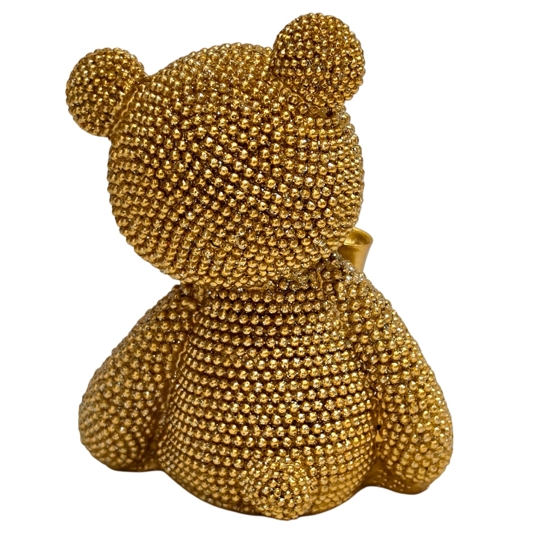 Statuina orsetto in resina dorata interamente ricoperta di brillantini glitterati, con fiocco raso oro al collo, occhi e naso neri e cuciture in rilievo sulle zampe. Oggetto decorativo scintillante firmato Sud Import, ideale come soprammobile glamour o idea regalo per bambini e occasioni speciali.
