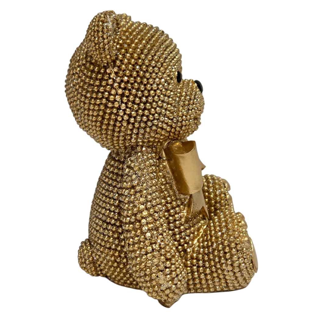 Statuina orsetto in resina dorata interamente ricoperta di brillantini glitterati, con fiocco raso oro al collo, occhi e naso neri e cuciture in rilievo sulle zampe. Oggetto decorativo scintillante firmato Sud Import, ideale come soprammobile glamour o idea regalo per bambini e occasioni speciali.
