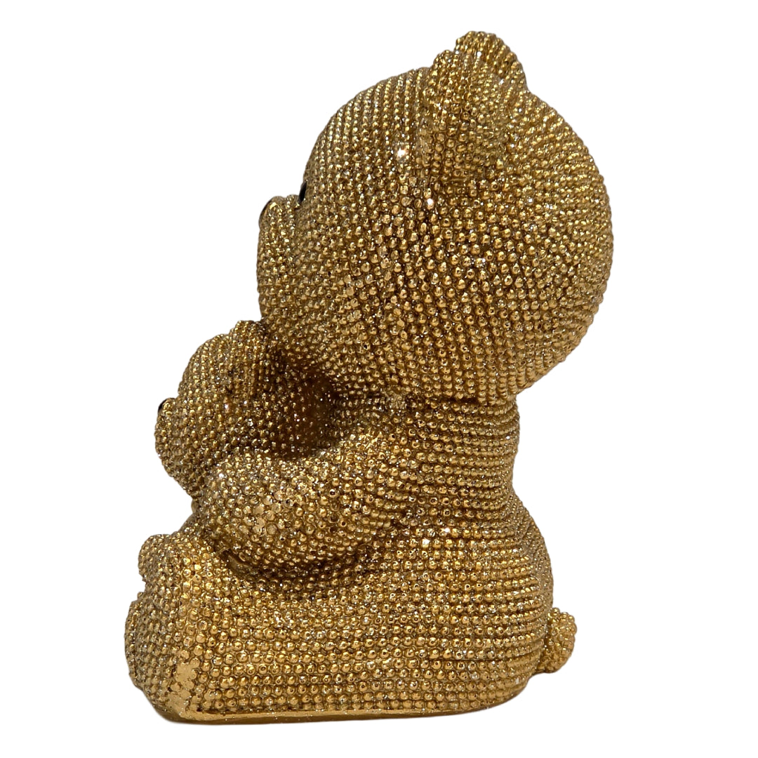 Statuina in resina raffigurante una coppia di orsetti dorati interamente ricoperti di brillantini glitterati, con l'orso più grande che abbraccia l'orsetto più piccolo seduto davanti a sé. Oggetto decorativo scintillante firmato Sud Import, ideale come soprammobile glamour o idea regalo per bambini e occasioni speciali.