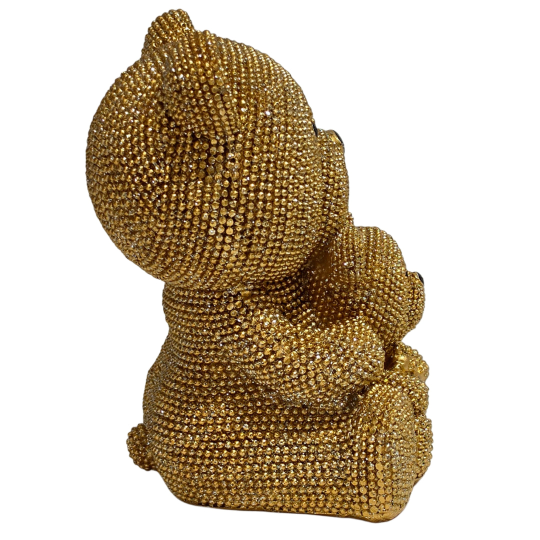 Statuina in resina raffigurante una coppia di orsetti dorati interamente ricoperti di brillantini glitterati, con l'orso più grande che abbraccia l'orsetto più piccolo seduto davanti a sé. Oggetto decorativo scintillante firmato Sud Import, ideale come soprammobile glamour o idea regalo per bambini e occasioni speciali.