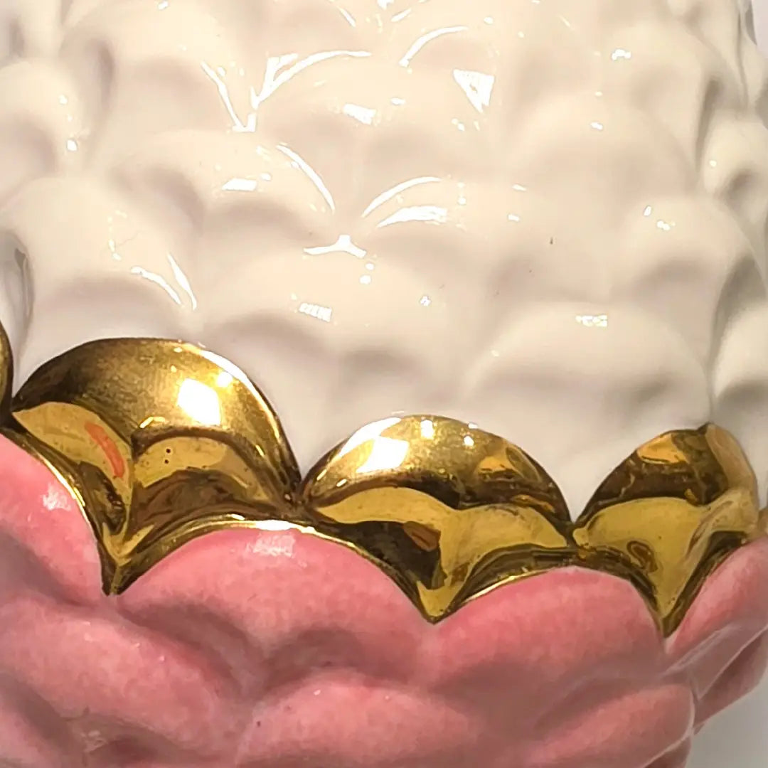 Pigna portafortuna in ceramica bicolore rosa e bianca lucida, impreziosita da una raffinata corona di squame dorate che ne definisce il profilo centrale. Questo elegante oggetto ornamentale artigianale poggia su una base circolare con finiture in oro, rappresentando un complemento d'arredo perfetto per decorazioni d'interni in stile chic e contemporaneo.