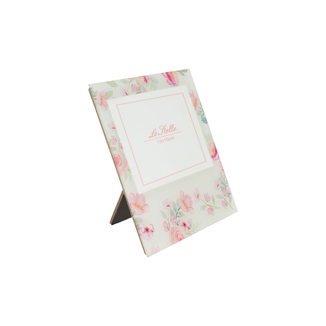 Una cornice portafoto in vetro, decorata con una delicata composizione di fiori rosa e foglie verdi acquerellate su fondo chiaro, che incornicia lo spazio centrale per la fotografia. La struttura è dotata di un cavalletto posteriore in legno, che ne permette il posizionamento su mensole o comodini. Un accessorio dal gusto romantico e delicato, perfetto come regalo o complemento d'arredo, che unisce eleganza e dolcezza floreale.