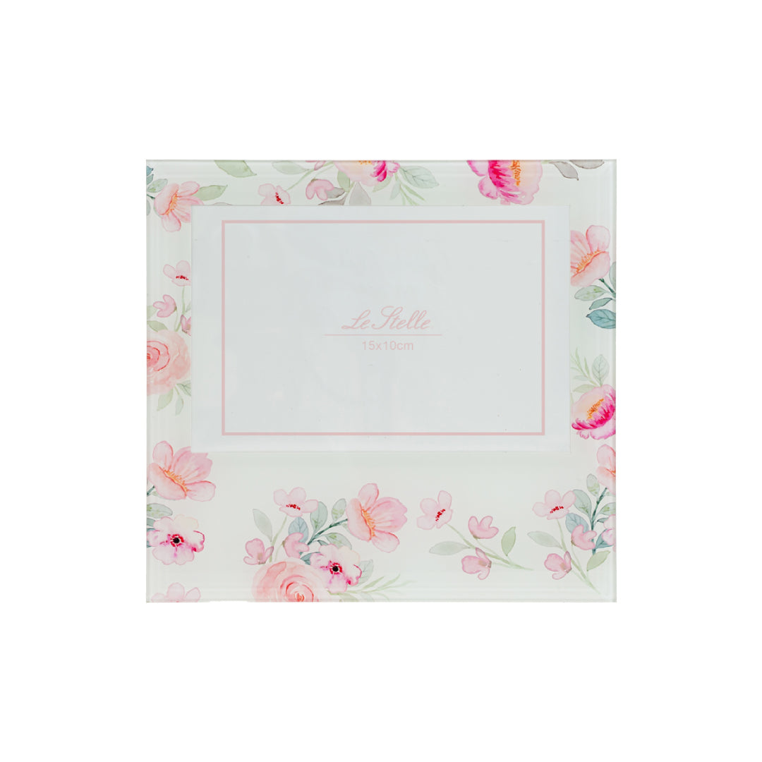 Una cornice portafoto in vetro, decorata con una delicata composizione di fiori rosa e foglie verdi acquerellate su fondo chiaro, che incornicia lo spazio centrale per la fotografia. La struttura è dotata di un cavalletto posteriore in legno, che ne permette il posizionamento su mensole o comodini. Un accessorio dal gusto romantico e delicato, perfetto come regalo o complemento d'arredo, che unisce eleganza e dolcezza floreale.