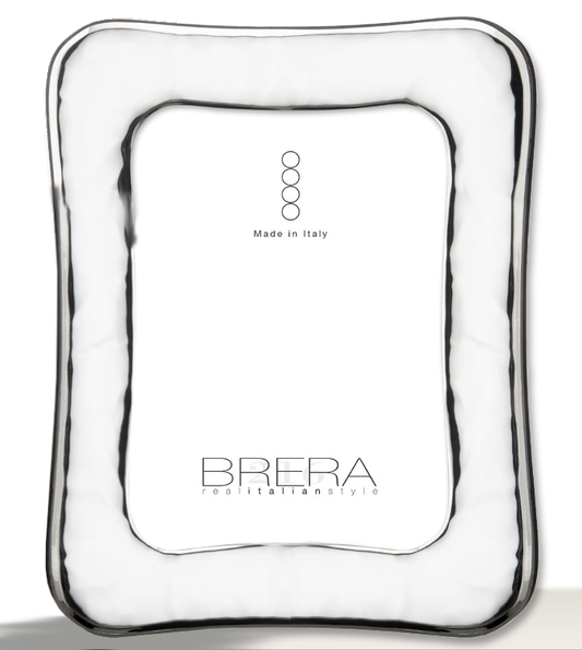 Portafoto da tavolo in argento bilaminato lucido con cornice sagomata e profilo ondulato. La superficie è caratterizzata da una lavorazione "stropicciata" o a effetto martellato morbido che crea riflessi luminosi dinamici. L'inserto centrale bianco riporta il marchio "BRERA real italian style" e la certificazione "Made in Italy".