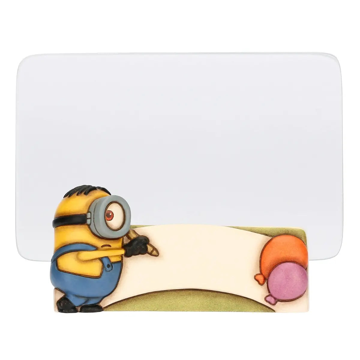 Cornice portafoto in ceramica Thun con personaggio Minion in rilievo. La base della cornice presenta un Minion con salopette azzurra intento a scrivere su una pergamena bianca, affiancato da due palloncini colorati. Design iconico Thun applicato al mondo dei Minions, ideale per camerette o come idea regalo originale.