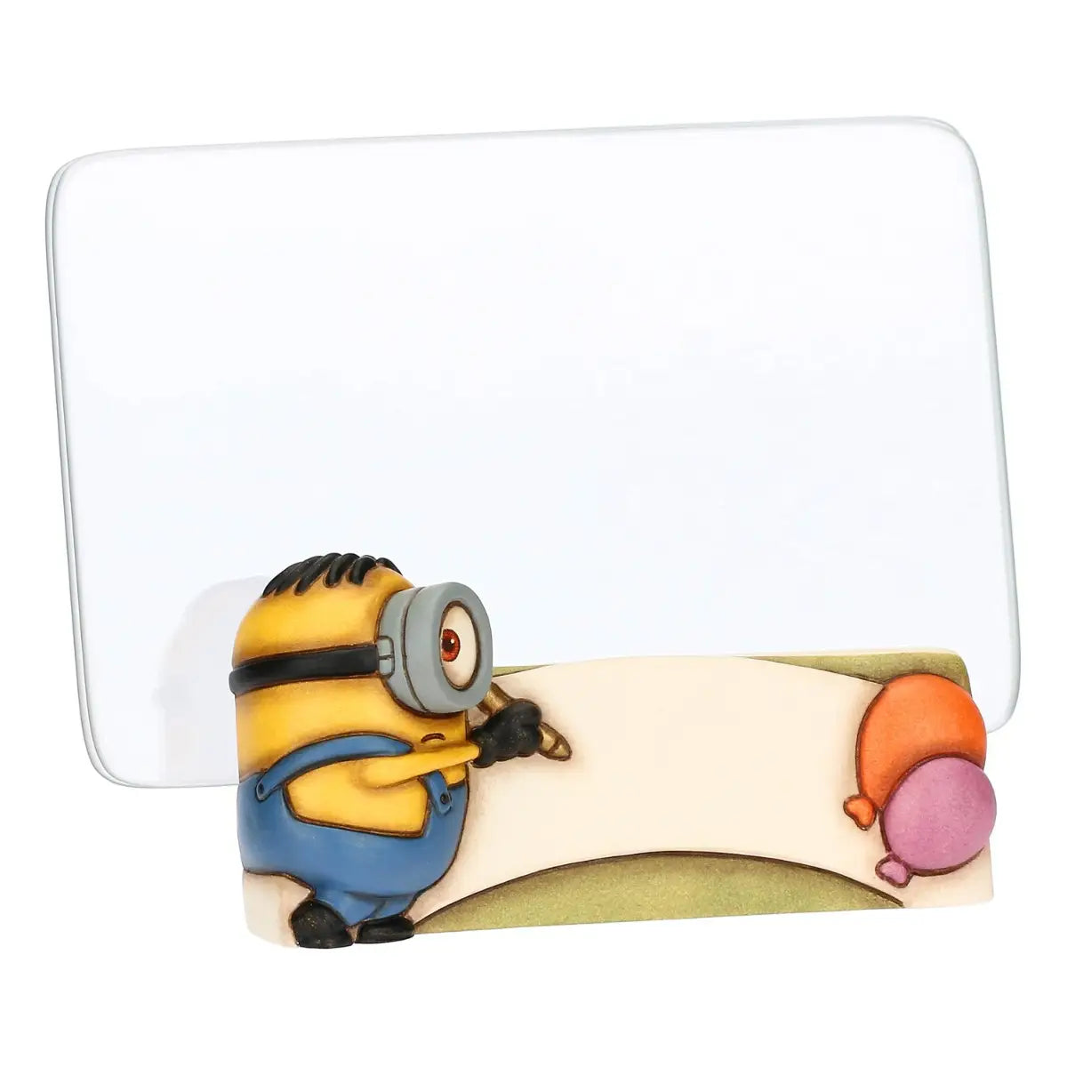 Cornice portafoto in ceramica Thun con personaggio Minion in rilievo. La base della cornice presenta un Minion con salopette azzurra intento a scrivere su una pergamena bianca, affiancato da due palloncini colorati. Design iconico Thun applicato al mondo dei Minions, ideale per camerette o come idea regalo originale.