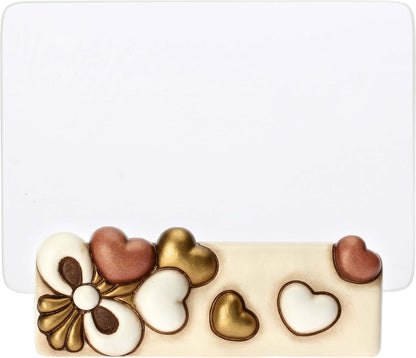 Il Portafoto con Cuori Thun presenta una base in ceramica decorata con cuori in rilievo e un'elegante lastra di vetro trasparente per esporre i tuoi ricordi più cari. Questo complemento d'arredo riflette lo stile inconfondibile del marchio Thun, ideale come preziosa idea regalo o come cornice decorativa per impreziosire la tua casa.
