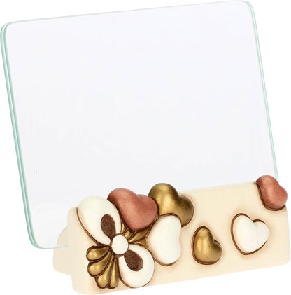 Il Portafoto con Cuori Thun presenta una base in ceramica decorata con cuori in rilievo e un'elegante lastra di vetro trasparente per esporre i tuoi ricordi più cari. Questo complemento d'arredo riflette lo stile inconfondibile del marchio Thun, ideale come preziosa idea regalo o come cornice decorativa per impreziosire la tua casa.