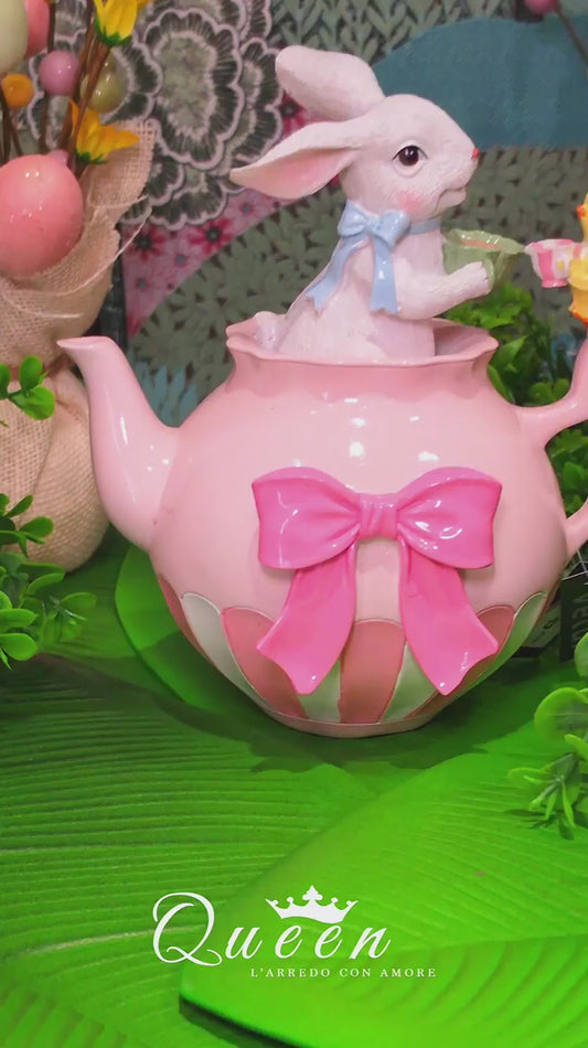 Decorazione pasquale Vetur in poliresina. Scenetta con coniglietto bianco con fiocco azzurro all'interno di una teiera rosa a righe con fiocco fucsia, mentre offre il tè a un piccolo pulcino. Altezza 20 cm.