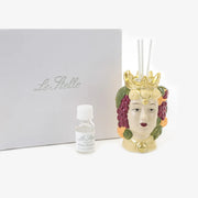 Profumatore d'ambiente in ceramica dipinta a mano raffigurante una testa di moro femminile con corona dorata, decorata con grappoli d'uva e agrumi colorati, con bastoncini bianchi e boccetta di fragranza "Home Fragrance". Diffusore dalla tradizione siciliana firmato Le Stelle, presentato con la sua confezione bianca del marchio, ideale come idea regalo raffinata.