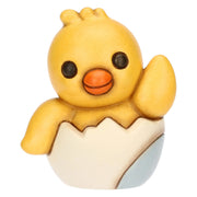 Statuina in ceramica Thun del Pulcino Polly, collezione Incanto di Pasqua. Il pulcino giallo è raffigurato mentre esce da un guscio d'uovo bianco e azzurro, con un'ala alzata in segno di saluto. Decorazione pasquale da collezione con i tipici tratti morbidi e i colori sfumati del marchio Thun.