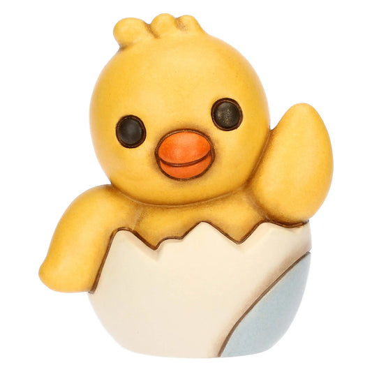 Statuina in ceramica Thun del Pulcino Polly, collezione Incanto di Pasqua. Il pulcino giallo è raffigurato mentre esce da un guscio d'uovo bianco e azzurro, con un'ala alzata in segno di saluto. Decorazione pasquale da collezione con i tipici tratti morbidi e i colori sfumati del marchio Thun.