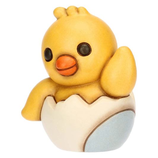 Statuina in ceramica Thun del Pulcino Polly, collezione Incanto di Pasqua. Il pulcino giallo è raffigurato mentre esce da un guscio d'uovo bianco e azzurro, con un'ala alzata in segno di saluto. Decorazione pasquale da collezione con i tipici tratti morbidi e i colori sfumati del marchio Thun.