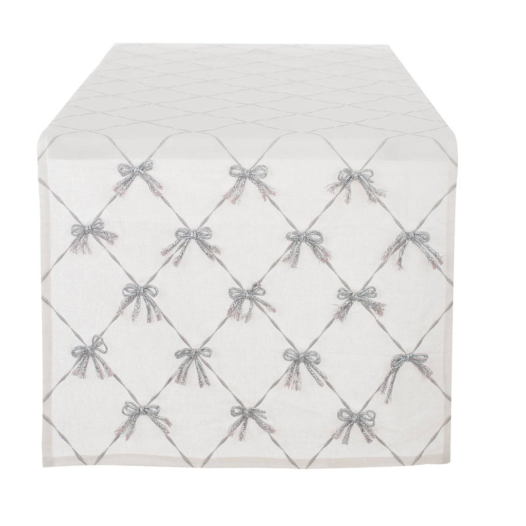 Runner Blanc Mariclò in tessuto bianco avorio con elegante ricamo a grata. All'incrocio delle linee spiccano piccoli fiocchi in rilievo color argento con dettagli sfrangiati molto raffinati.