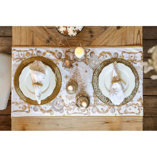 Tavola elegante con runner Blanc Mariclò Magia d'Oro su legno rustico. Mise en place con piatti bianchi, sottopiatti dorati e tovaglioli coordinati. Atmosfera natalizia impreziosita da candele.