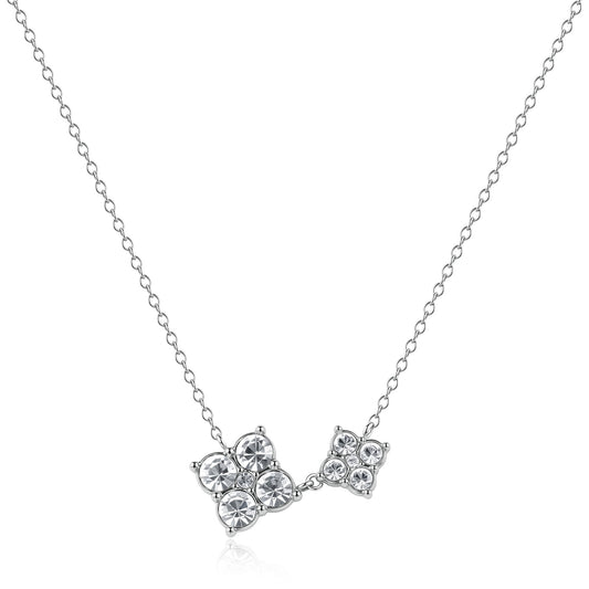 Collana S'Agapõ in acciaio lucido della linea Gleam, composta da una sottile catenina e un pendente asimmetrico formato da due fiori stilizzati di diverse dimensioni, entrambi impreziositi da quattro cristalli bianchi circolari.