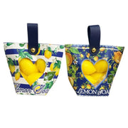 Saponetta al limone a forma di agrume custodita all'interno di una graziosa borsetta regalo assortita con manico in finta pelle blu firmata La Divina Costiera. Una confezione decorativa con finestra trasparente a forma di cuore e motivi ispirati ad Amalfi e alla Sicilia, ideale come profumata bomboniera o originale idea regalo per la cura del corpo.