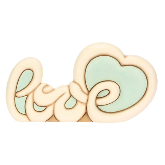 L'immagine mostra un soprammobile in ceramica che raffigura la parola "Love" (amore) scritta in uno stile corsivo morbido, tondeggiante e stilizzato, tipico del design Thun.