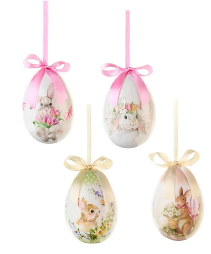 Set da 4 uova decorative della collezione "Dorothy" di Nuvole di Stoffa, pensate come addobbi pasquali da appendere per l'albero di Pasqua o per creare composizioni primaverili. Ogni uovo presenta illustrazioni in stile acquerello con teneri coniglietti, fiori, tulipani e margherite, rifinito nella parte superiore da un elegante nastro in raso con fiocco nei toni del rosa e del panna.