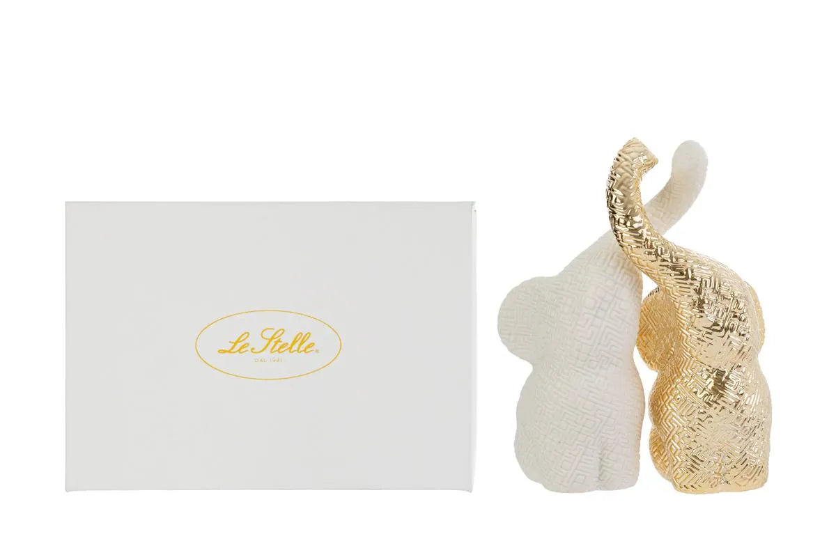 Set di due elefantini decorativi in porcellana bianco e oro firmati Le Stelle, caratterizzati da una finitura lucida impreziosita da una trama geometrica a rilievo con effetto 3D e trombe sollevate che si incrociano. Queste due raffinate statuine di elefanti di design rappresentano un complemento d'arredo moderno e portafortuna, ideale come bomboniera di classe o originale oggetto ornamentale per la casa.