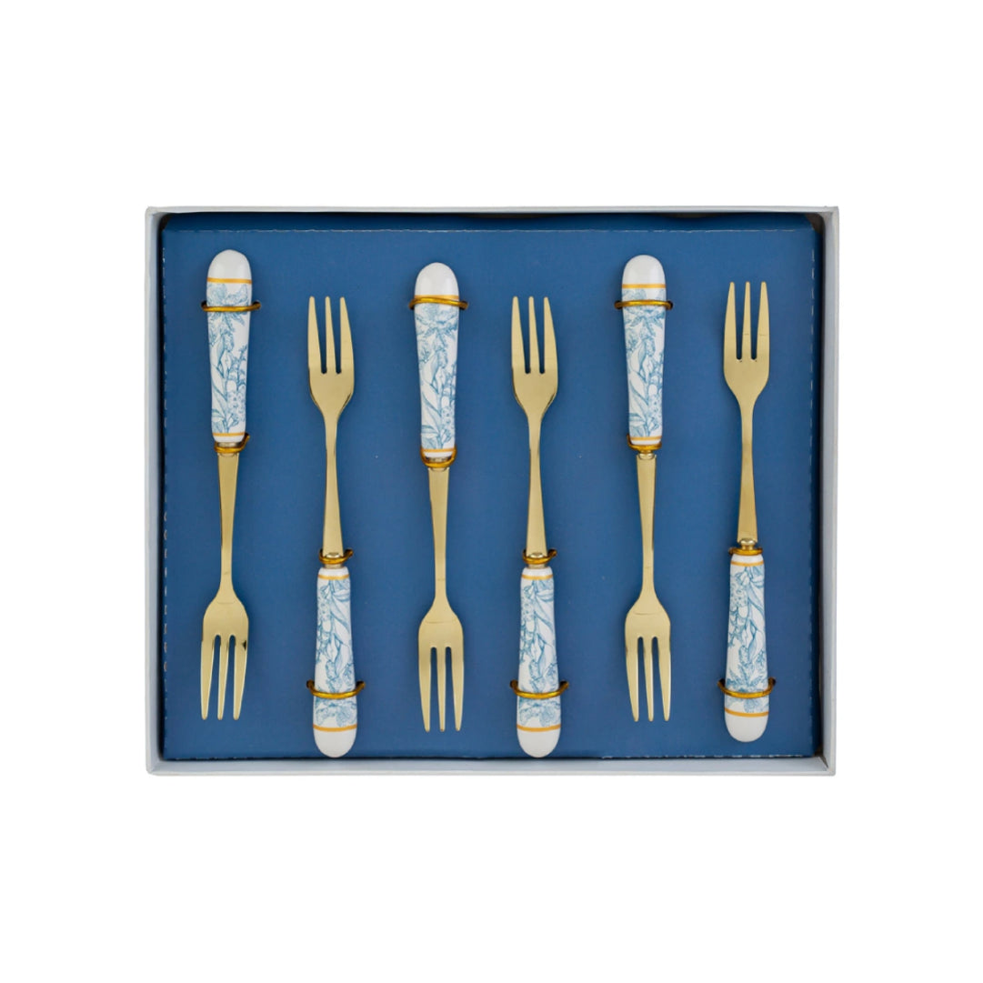 Set di 6 forchettine da dolce con decoro azzurro firmato Le Stelle, caratterizzato da rebbi in metallo color oro e raffinati manici in porcellana bianca decorati con delicati motivi floreali azzurri. Questo elegante servizio di posate da dessert di design è accompagnato dalla sua scatola regalo quadrata coordinata con la stessa fantasia botanica, perfetto come bomboniera di classe o idea regalo home decor.