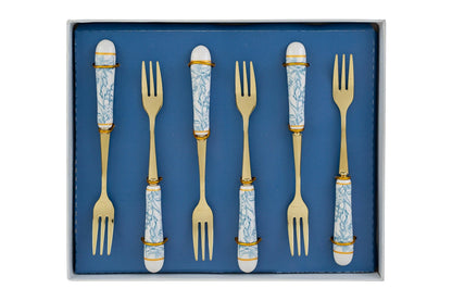 Set di 6 forchettine da dolce con decoro azzurro firmato Le Stelle, caratterizzato da rebbi in metallo color oro e raffinati manici in porcellana bianca decorati con delicati motivi floreali azzurri. Questo elegante servizio di posate da dessert di design è accompagnato dalla sua scatola regalo quadrata coordinata con la stessa fantasia botanica, perfetto come bomboniera di classe o idea regalo home decor.