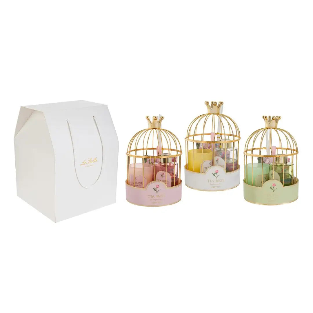 Set regalo assortito firmato Le Stelle composto da una candela in vetro e un profumatore per ambienti con bastoncini, presentati in un'elegante gabbia dorata con corona decorativa. Questa raffinata idea regalo o bomboniera per eventi è disponibile nei colori rosa, giallo e verde e include una graziosa busta shopper bianca coordinata.