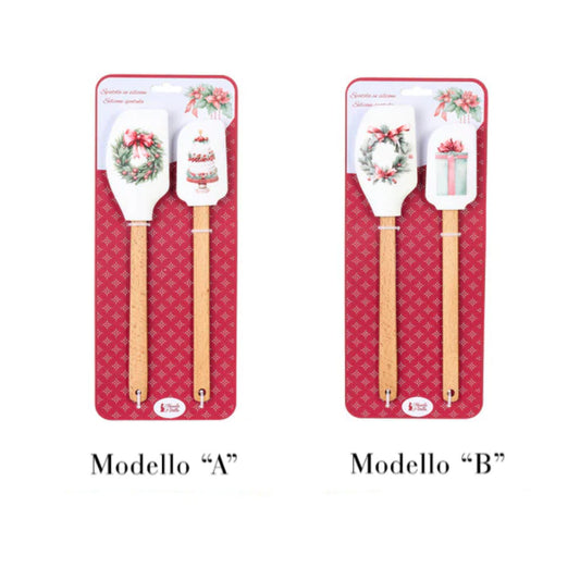 Due varianti di set regalo composti da due spatole in silicone con manico in legno Nuvole di Stoffa. Il Modello A presenta illustrazioni di una ghirlanda natalizia e una torta a piani; il Modello B mostra una ghirlanda di pino con bacche e un pacco regalo azzurro. Entrambi i set sono confezionati su un cartoncino rosso decorato.