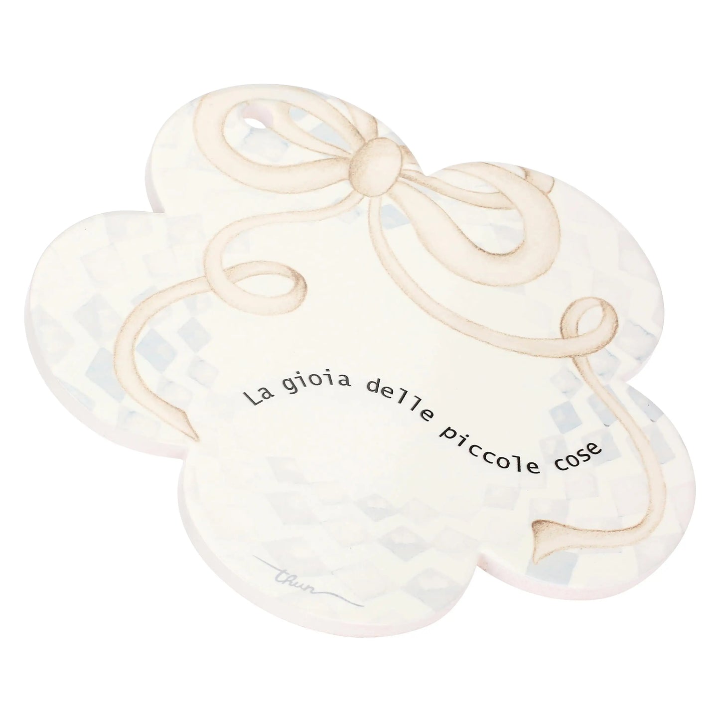 Questa immagine mostra il sottopentola in porcellana a forma di fiore visto da una prospettiva angolata e leggermente rialzata, che ne mette in risalto lo spessore e la finitura levigata.

L'inquadratura di tre quarti permette di osservare la curvatura dei cinque petali e il bordo bianco e uniforme della ceramica. La decorazione sulla superficie, che comprende il morbido fiocco beige annodato in alto e la scritta centrale "La gioia delle piccole cose"