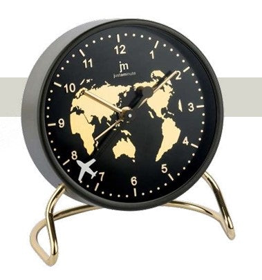 Sveglia da tavolo circolare Justaminute con tema "Planisfero Dorato". Il quadrante nero opaco presenta una mappa del mondo stilizzata in oro lucido al centro. I numeri arabi e le lancette sono dorati, mentre un piccolo aeroplano bianco funge da dettaglio decorativo sulla scala dei minuti. La struttura è sostenuta da un elegante supporto a cavalletto in metallo dorato.
