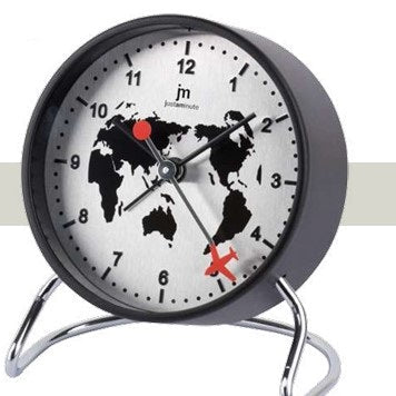 Sveglia da tavolo circolare Justaminute con tema "Planisfero Nero". Il quadrante argentato con finitura spazzolata presenta una mappa del mondo stilizzata in nero. I numeri arabi e le lancette sono neri, mentre la lancetta della sveglia e un dettaglio a forma di aeroplano sulla lancetta dei secondi sono di un vivace colore rosso. La struttura è sostenuta da un supporto a cavalletto in metallo cromato lucido.
