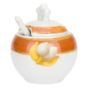 La Zuccheriera con Cucchiaio Tulipani è un elegante accessorio in porcellana bianca decorato con pennellate ambra e un tulipano in rilievo dalle foglie dorate. Il set include un pratico cucchiaino coordinato con la scritta "caffè al volo", rendendolo un complemento d'arredo funzionale e una perfetta idea regalo per amanti del design floreale.