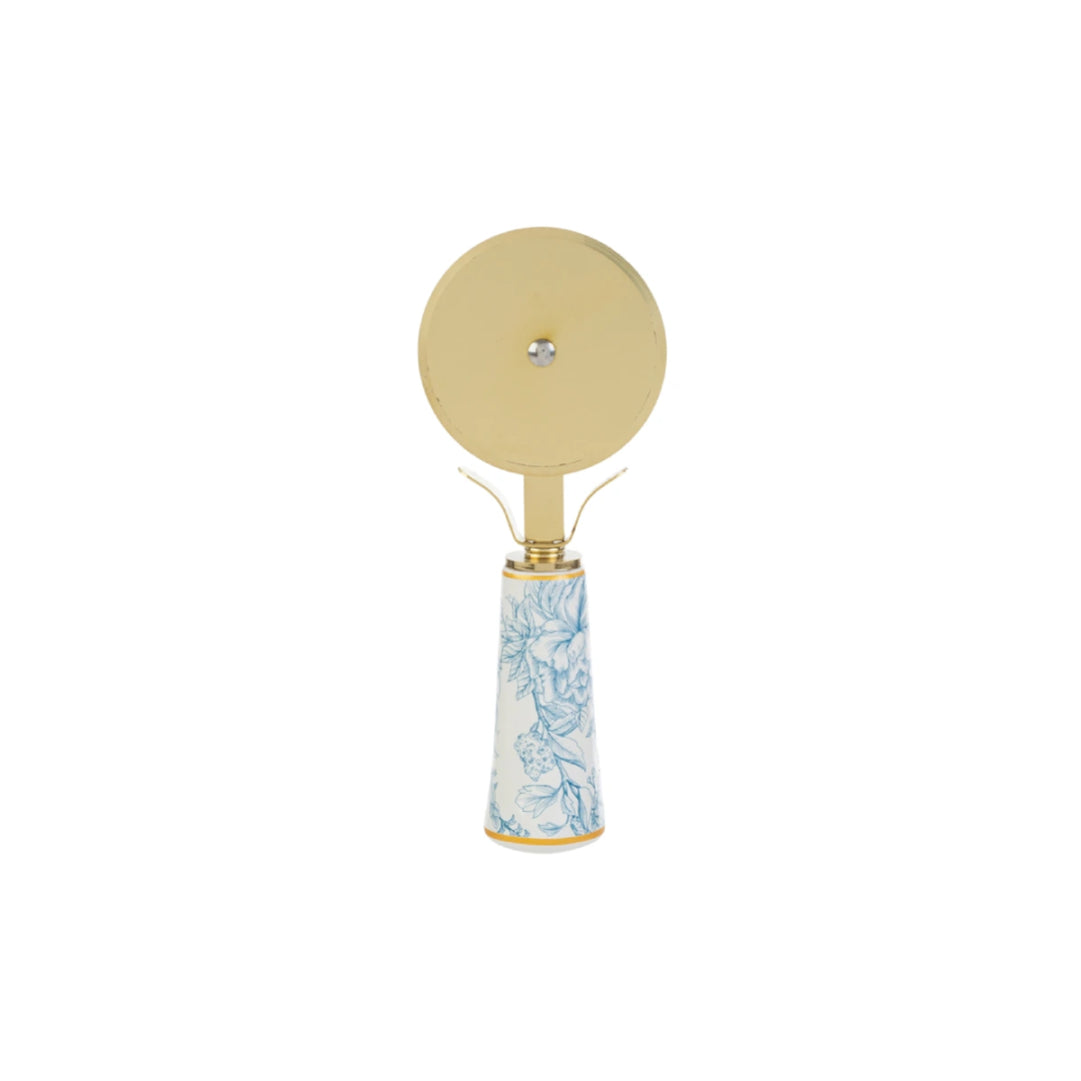 Tagliapizza con decoro azzurro firmato Le Stelle, caratterizzato da una lama rotante circolare in metallo color oro e un elegante manico in porcellana bianca decorato con delicati motivi floreali celestini. Questo raffinato utensile da cucina di design è accompagnato dalla sua custodia regalo rettangolare coordinata con la stessa fantasia botanica, perfetto come bomboniera di classe o idea regalo home decor.
