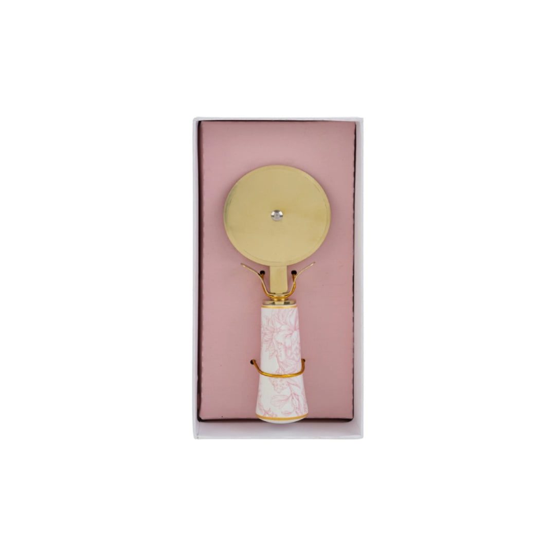Tagliapizza con decoro rosa firmato Le Stelle, caratterizzato da una lama rotante circolare in metallo color oro e un elegante manico in porcellana bianca decorato con delicati motivi floreali rosati. Questo raffinato utensile da cucina di design è accompagnato dalla sua custodia regalo rettangolare coordinata con la stessa fantasia botanica, perfetto come bomboniera di classe o idea regalo home decor.