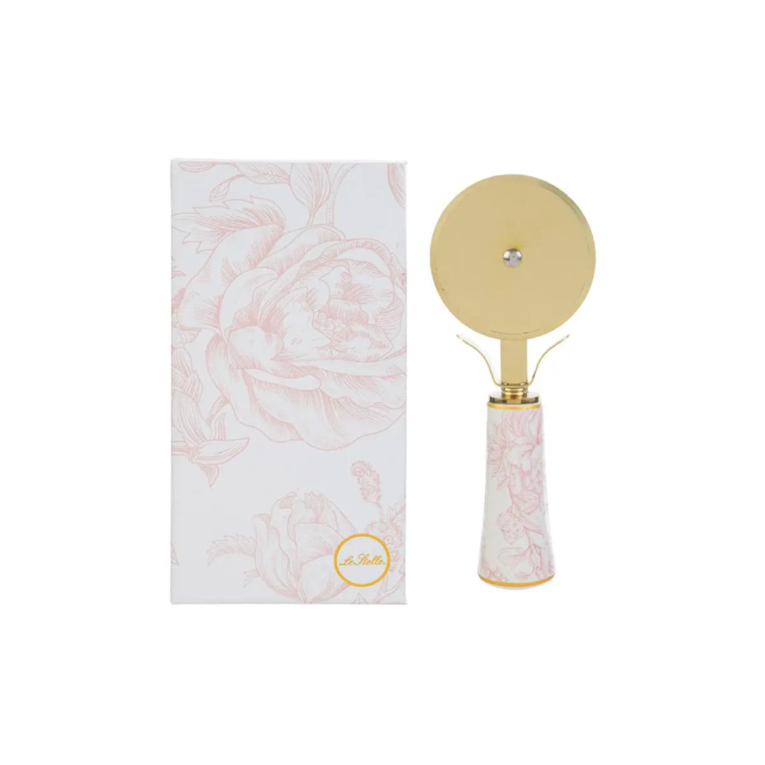 Tagliapizza con decoro rosa firmato Le Stelle, caratterizzato da una lama rotante circolare in metallo color oro e un elegante manico in porcellana bianca decorato con delicati motivi floreali rosati. Questo raffinato utensile da cucina di design è accompagnato dalla sua custodia regalo rettangolare coordinata con la stessa fantasia botanica, perfetto come bomboniera di classe o idea regalo home decor.