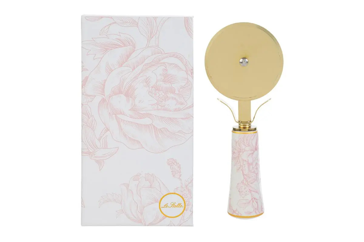 Tagliapizza con decoro rosa firmato Le Stelle, caratterizzato da una lama rotante circolare in metallo color oro e un elegante manico in porcellana bianca decorato con delicati motivi floreali rosati. Questo raffinato utensile da cucina di design è accompagnato dalla sua custodia regalo rettangolare coordinata con la stessa fantasia botanica, perfetto come bomboniera di classe o idea regalo home decor.