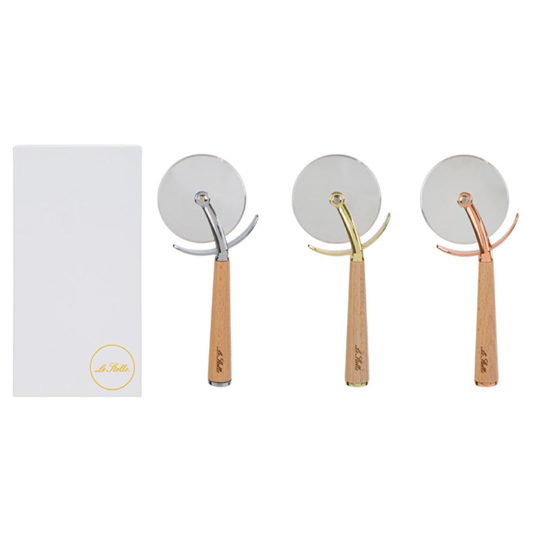 Tagliapizza con rotella in acciaio inox e manico in legno chiaro inciso "Le Stelle", disponibile in tre finiture assortite argento, oro e rosé, presentato accanto alla sua confezione bianca con logo del marchio. Utensile da cucina pratico ed elegante, ideale come bomboniera o idea regalo raffinata.