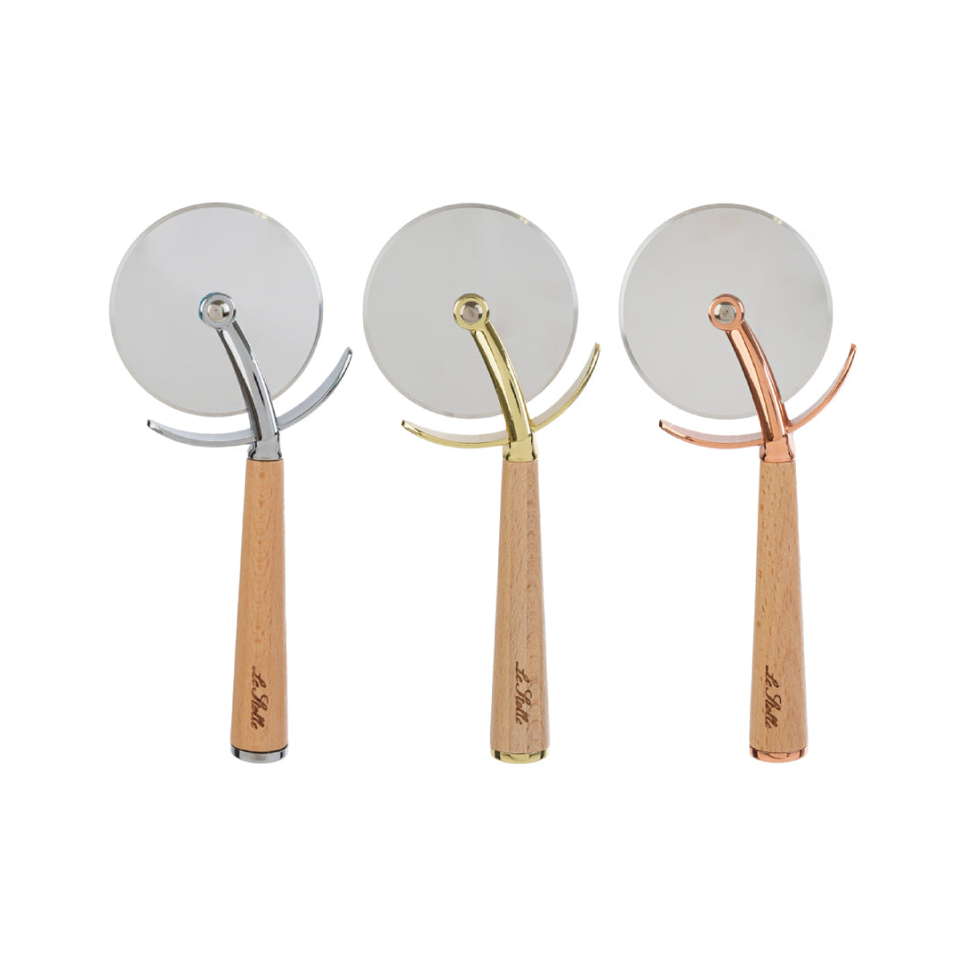 Tagliapizza con rotella in acciaio inox e manico in legno chiaro inciso "Le Stelle", disponibile in tre finiture assortite argento, oro e rosé, presentato accanto alla sua confezione bianca con logo del marchio. Utensile da cucina pratico ed elegante, ideale come bomboniera o idea regalo raffinata.