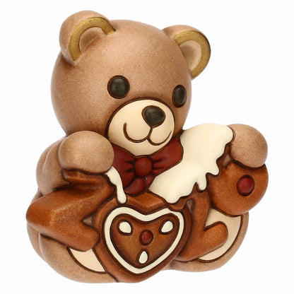 Statuetta in ceramica raffigurante un orsetto frontale con un’espressione dolce, che indossa un papillon rosso scuro. L'orso tiene tra le zampe la scritta "2026" realizzata in uno stile che ricorda un biscotto di pan di zenzero, con glassa bianca colante e un cuore decorato al centro al posto dello zero. I dettagli includono grandi occhi neri, un muso color crema e l'interno delle orecchie rifinito in oro, conferendo un aspetto festivo e cerimoniale alla figura.