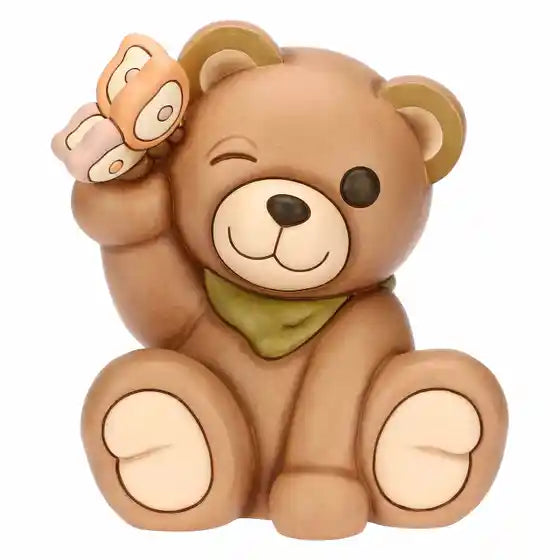 Statuina maxi in ceramica dipinta a mano raffigurante il classico orsetto Teddy di Thun. L'orso è seduto in posa sorridente con un occhio chiuso in un occhiolino, indossa un fazzoletto verde al collo e tiene una farfalla rosa e arancione appoggiata sull'orecchio destro sollevato. Design caratterizzato dalle tipiche forme morbide e dai colori caldi del brand.