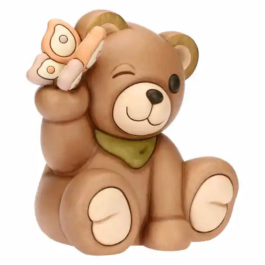 Statuina maxi in ceramica dipinta a mano raffigurante il classico orsetto Teddy di Thun. L'orso è seduto in posa sorridente con un occhio chiuso in un occhiolino, indossa un fazzoletto verde al collo e tiene una farfalla rosa e arancione appoggiata sull'orecchio destro sollevato. Design caratterizzato dalle tipiche forme morbide e dai colori caldi del brand.