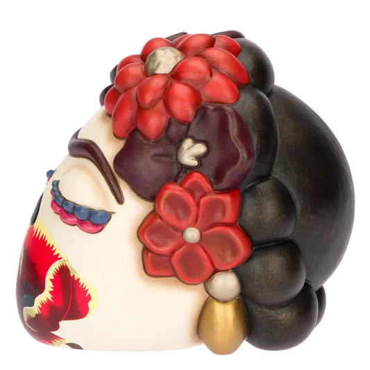Scultura decorativa in ceramica Thun raffigurante la testa di Frida Kahlo in stile "calavera", caratterizzata da occhi chiusi con ciglia colorate, l'iconico sopracciglio unico e un grande papavero rosso dipinto sul volto. Questa creazione artistica è riccamente adornata da fiori rossi e bordeaux tra i capelli castani, rappresentando un pezzo da collezione unico che celebra l'estetica e la forza della celebre pittrice messicana.