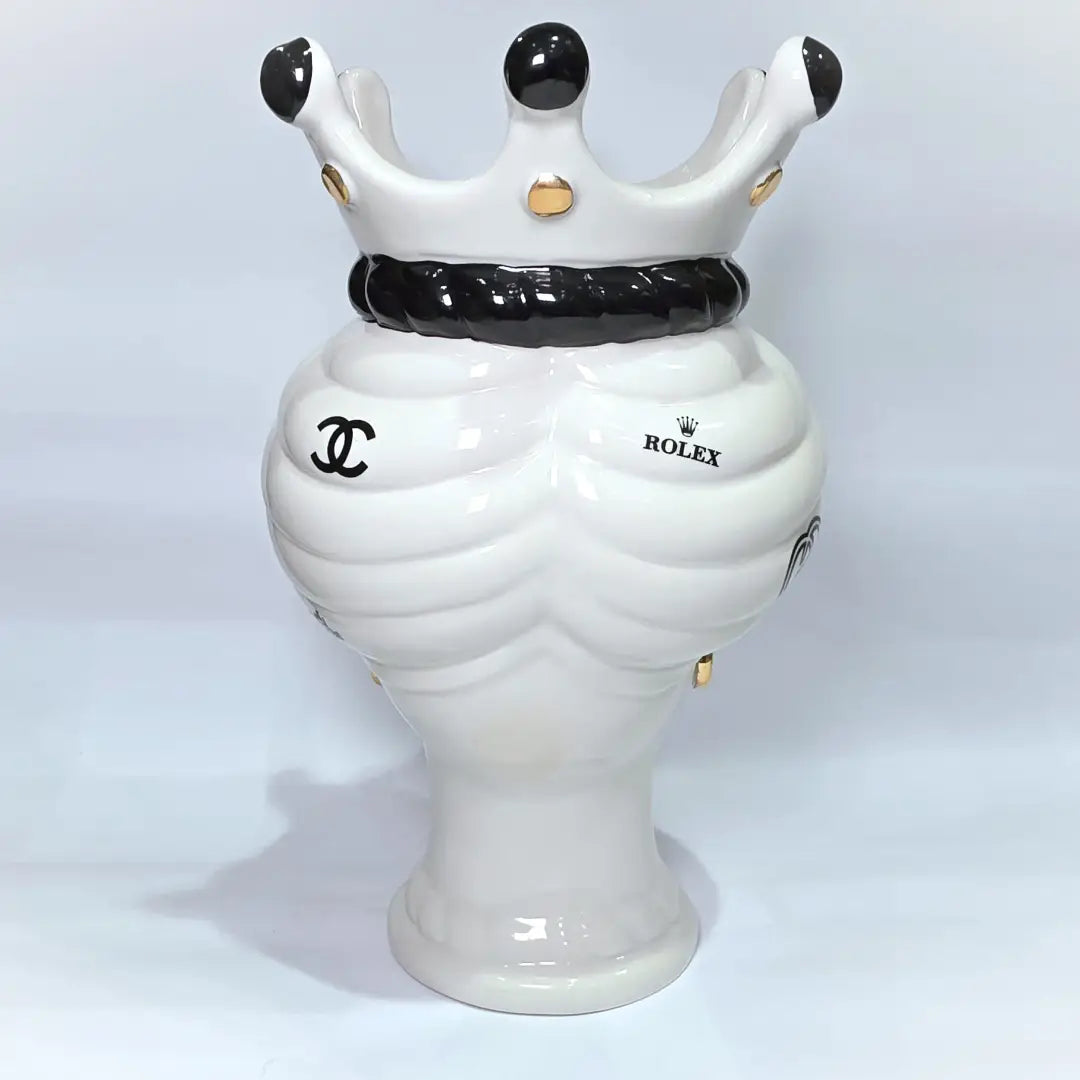 Coppia di Teste di Moro in ceramica bianca lucida con turbanti neri e bianchi decorati da loghi fashion neri e dorati, completate da corone regali e labbra con finitura in oro zecchino. Queste sculture ornamentali di design pop art fondono la tradizione ceramica siciliana con l'estetica del lusso moderno, rappresentando un complemento d'arredo audace ed esclusivo per interni ricercati.