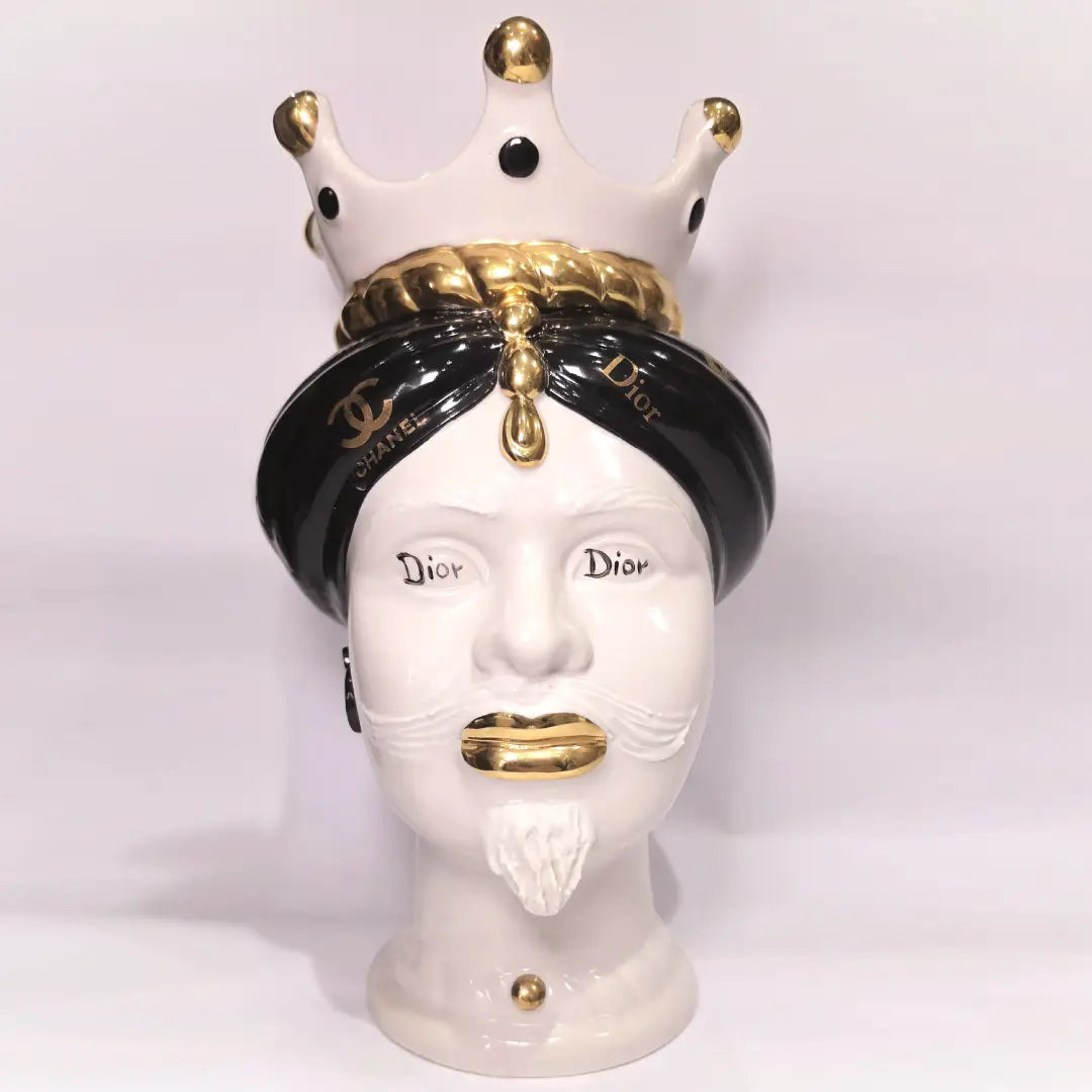 Coppia di Teste di Moro in ceramica bianca lucida con turbanti neri e bianchi decorati da loghi fashion neri e dorati, completate da corone regali e labbra con finitura in oro zecchino. Queste sculture ornamentali di design pop art fondono la tradizione ceramica siciliana con l'estetica del lusso moderno, rappresentando un complemento d'arredo audace ed esclusivo per interni ricercati.