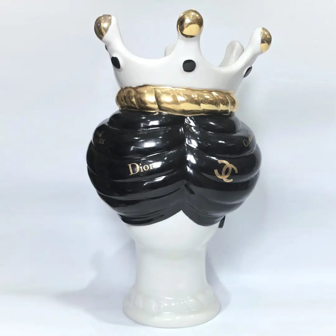 Coppia di Teste di Moro in ceramica bianca lucida con turbanti neri e bianchi decorati da loghi fashion neri e dorati, completate da corone regali e labbra con finitura in oro zecchino. Queste sculture ornamentali di design pop art fondono la tradizione ceramica siciliana con l'estetica del lusso moderno, rappresentando un complemento d'arredo audace ed esclusivo per interni ricercati.