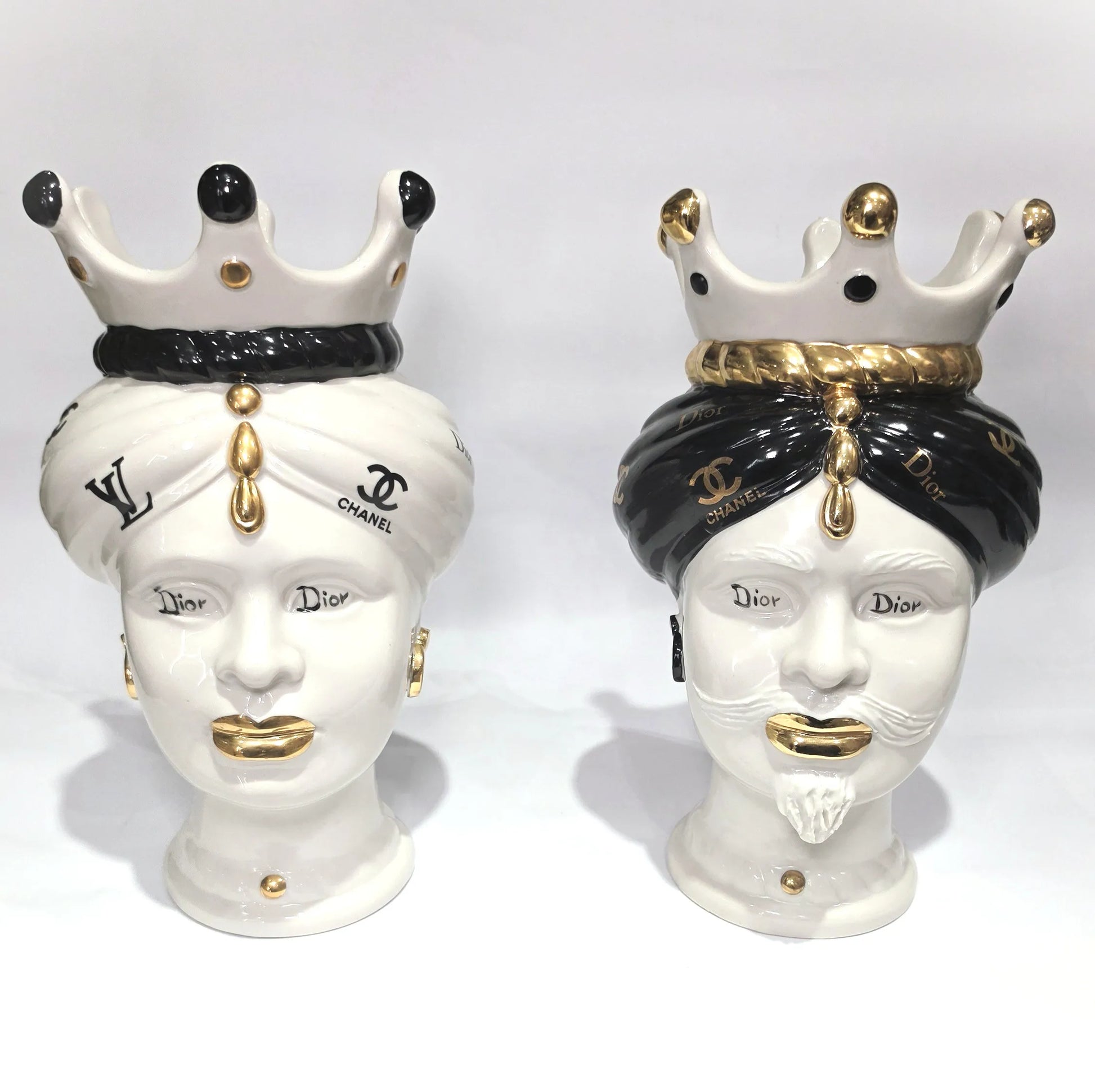 Coppia di Teste di Moro in ceramica bianca lucida con turbanti neri e bianchi decorati da loghi fashion neri e dorati, completate da corone regali e labbra con finitura in oro zecchino. Queste sculture ornamentali di design pop art fondono la tradizione ceramica siciliana con l'estetica del lusso moderno, rappresentando un complemento d'arredo audace ed esclusivo per interni ricercati.