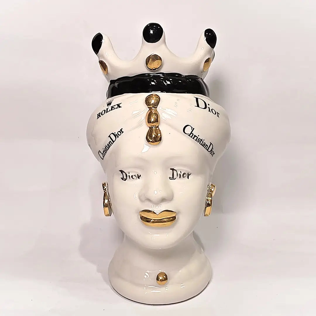 Coppia di Teste di Moro in ceramica bianca lucida con turbanti neri e bianchi decorati da loghi fashion neri e dorati, completate da corone regali e labbra con finitura in oro zecchino. Queste sculture ornamentali di design pop art fondono la tradizione ceramica siciliana con l'estetica del lusso moderno, rappresentando un complemento d'arredo audace ed esclusivo per interni ricercati.