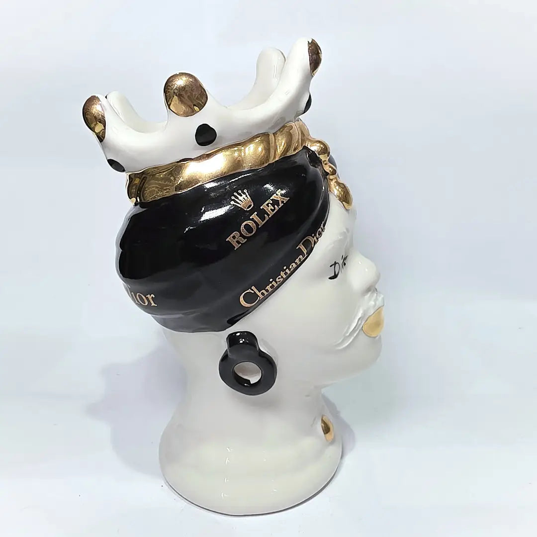 Coppia di Teste di Moro in ceramica bianca lucida con turbanti neri e bianchi decorati da loghi fashion neri e dorati, completate da corone regali e labbra con finitura in oro zecchino. Queste sculture ornamentali di design pop art fondono la tradizione ceramica siciliana con l'estetica del lusso moderno, rappresentando un complemento d'arredo audace ed esclusivo per interni ricercati.